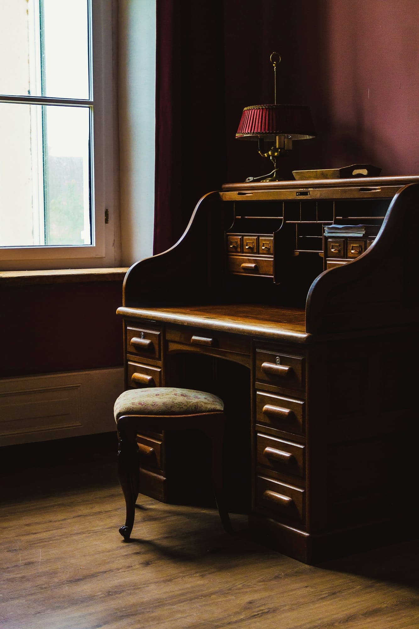 A roll-top desk in a lamplit study with a red wall