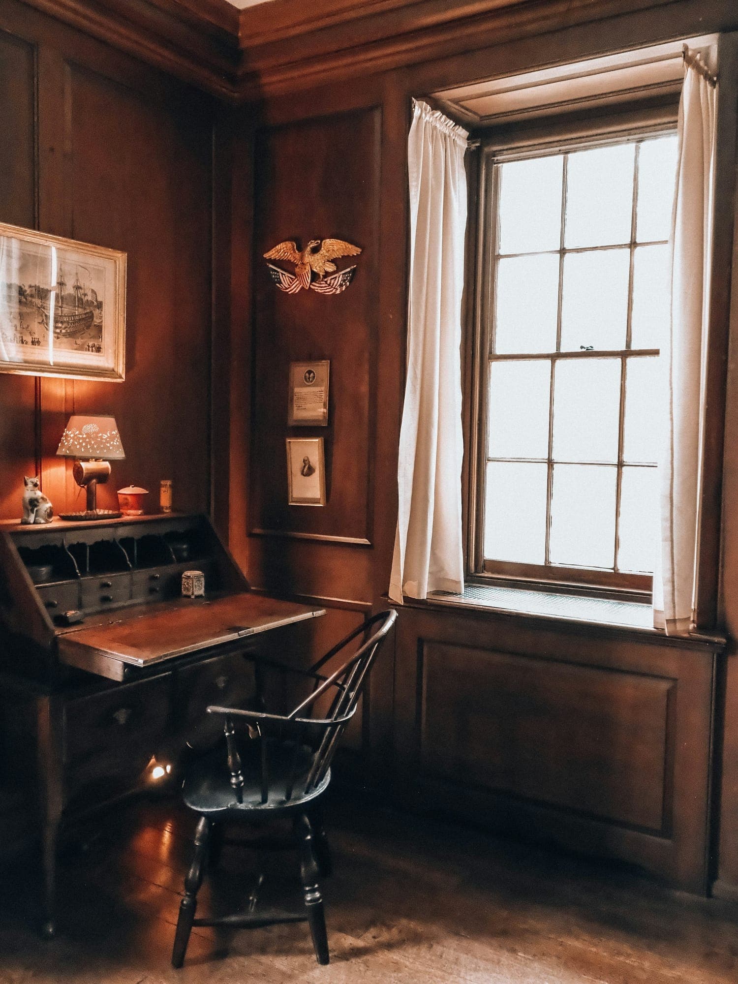 A writing desk in a wood-paneled study lit by a window