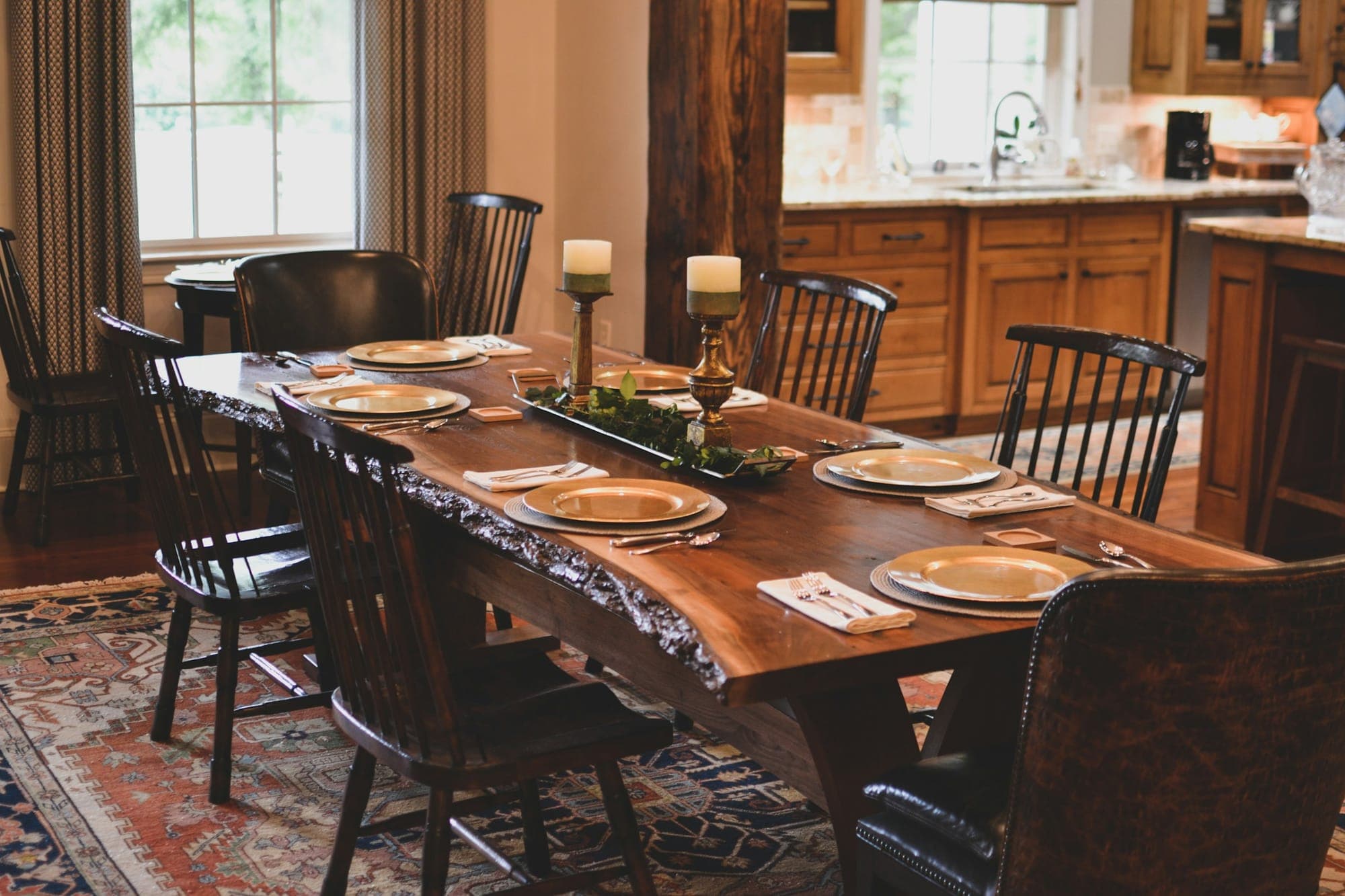 A live-edge walnut slab dining table on a trestle base, set for eight, in a family kitchen