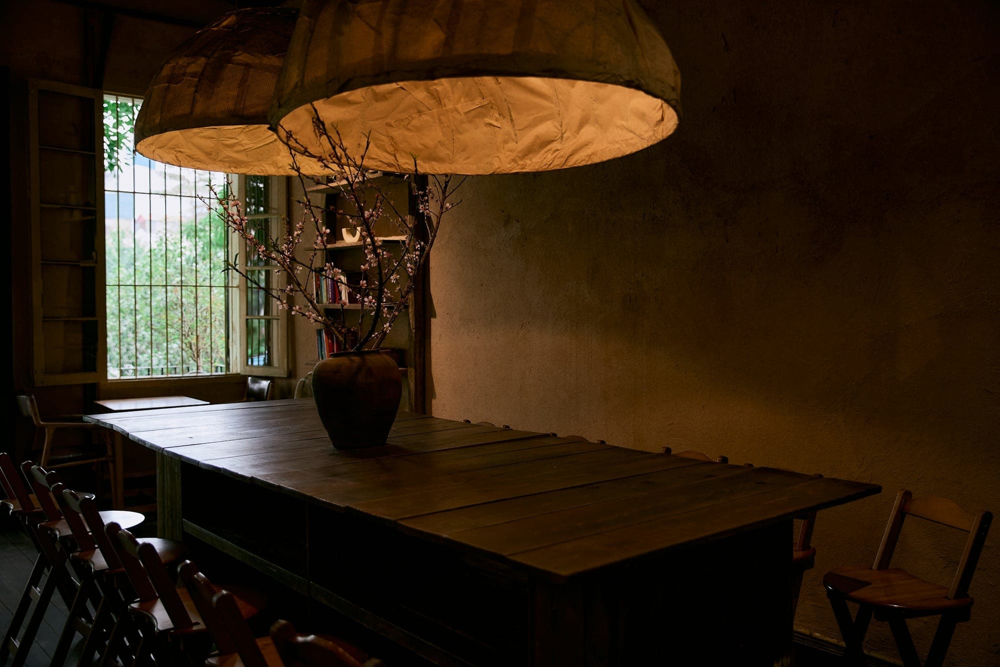 A substantial plank-top dining table under paper lanterns