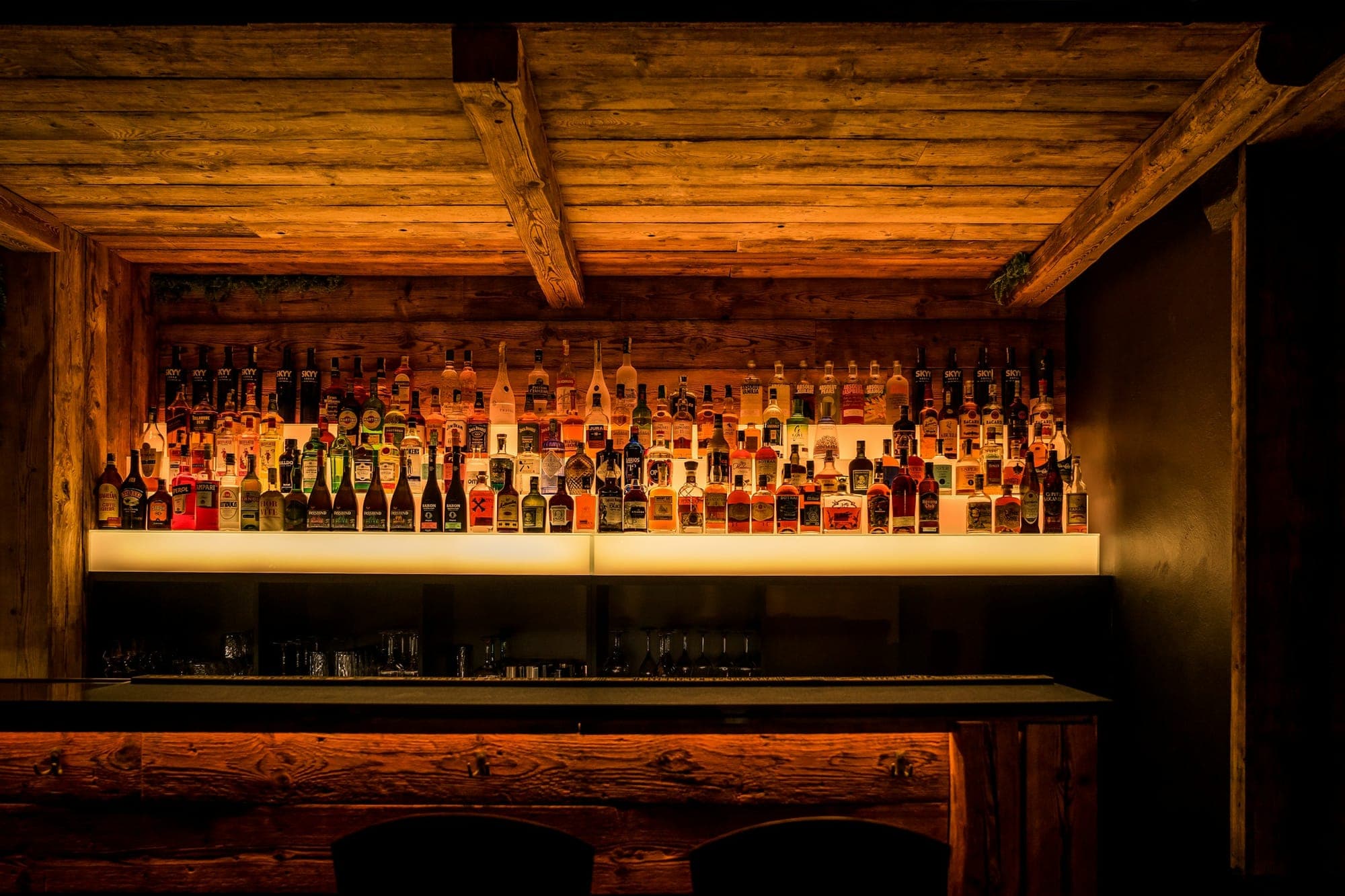 A home bar with a backlit wall of bottles and a hardwood counter